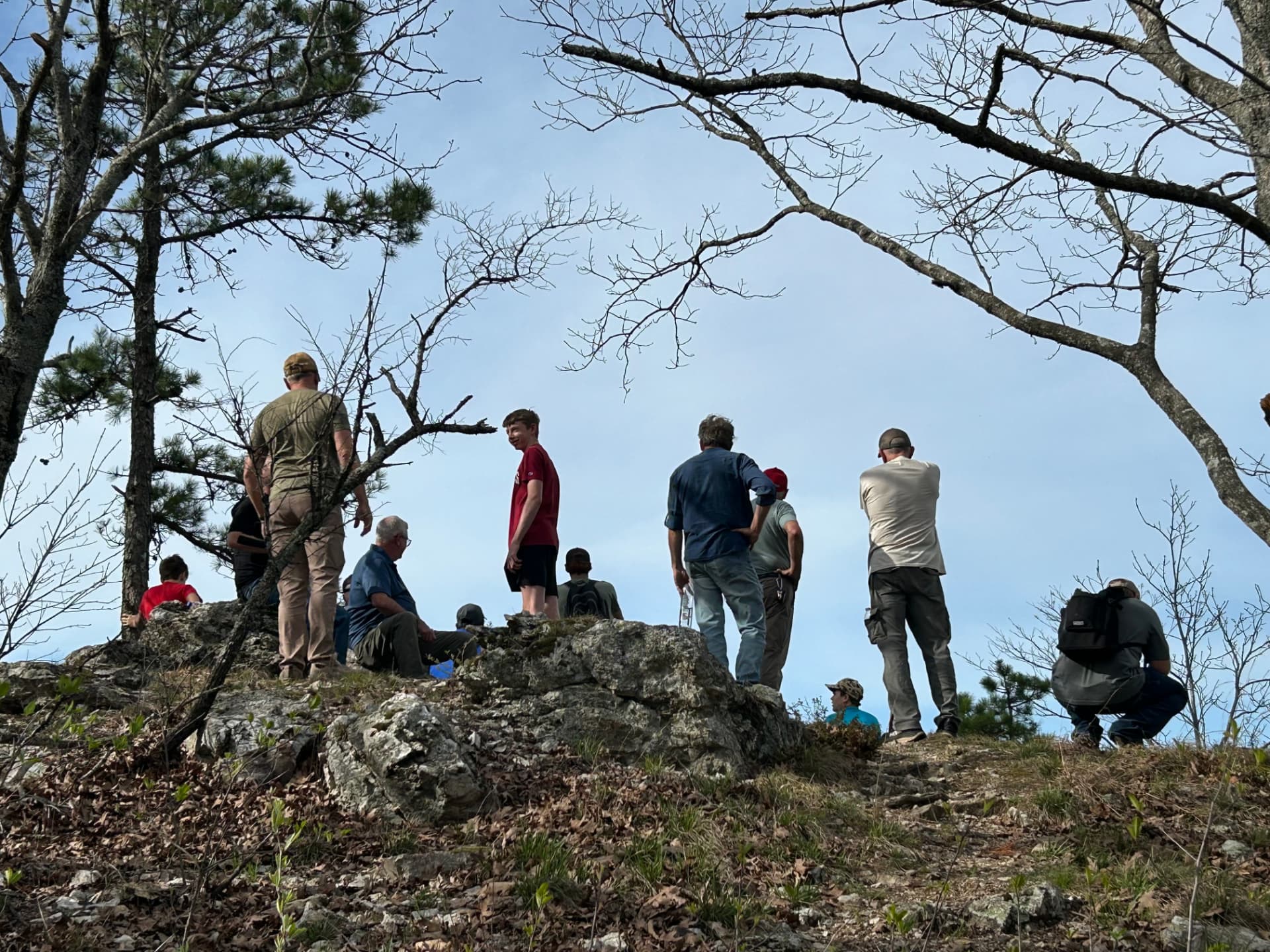 Men and boys gathered on a rocky bluff under the pines