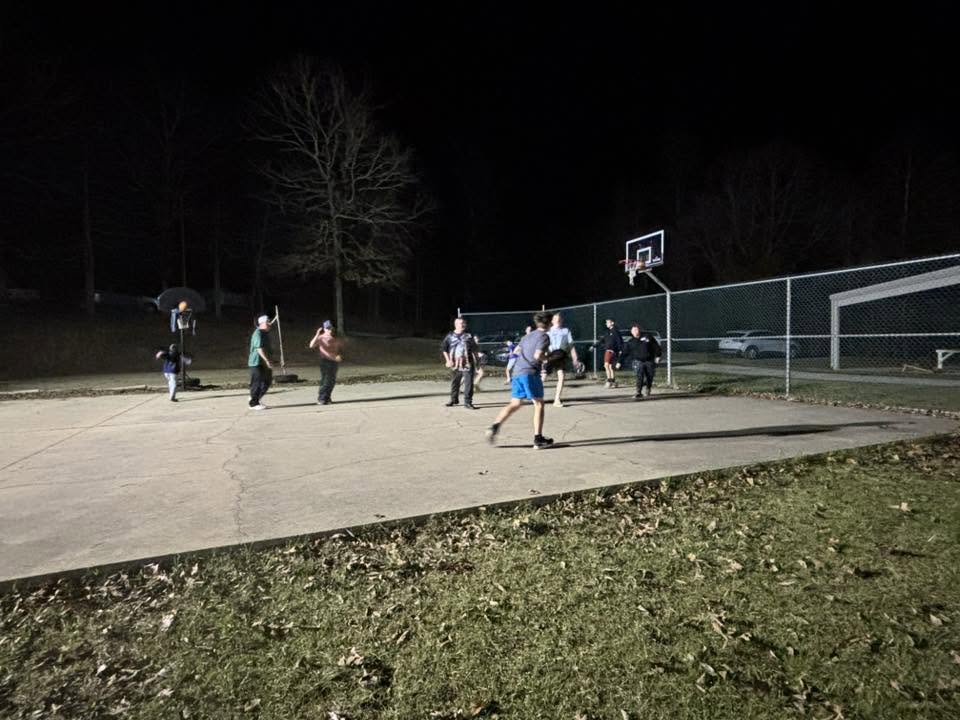 Men playing basketball under the lights after dark